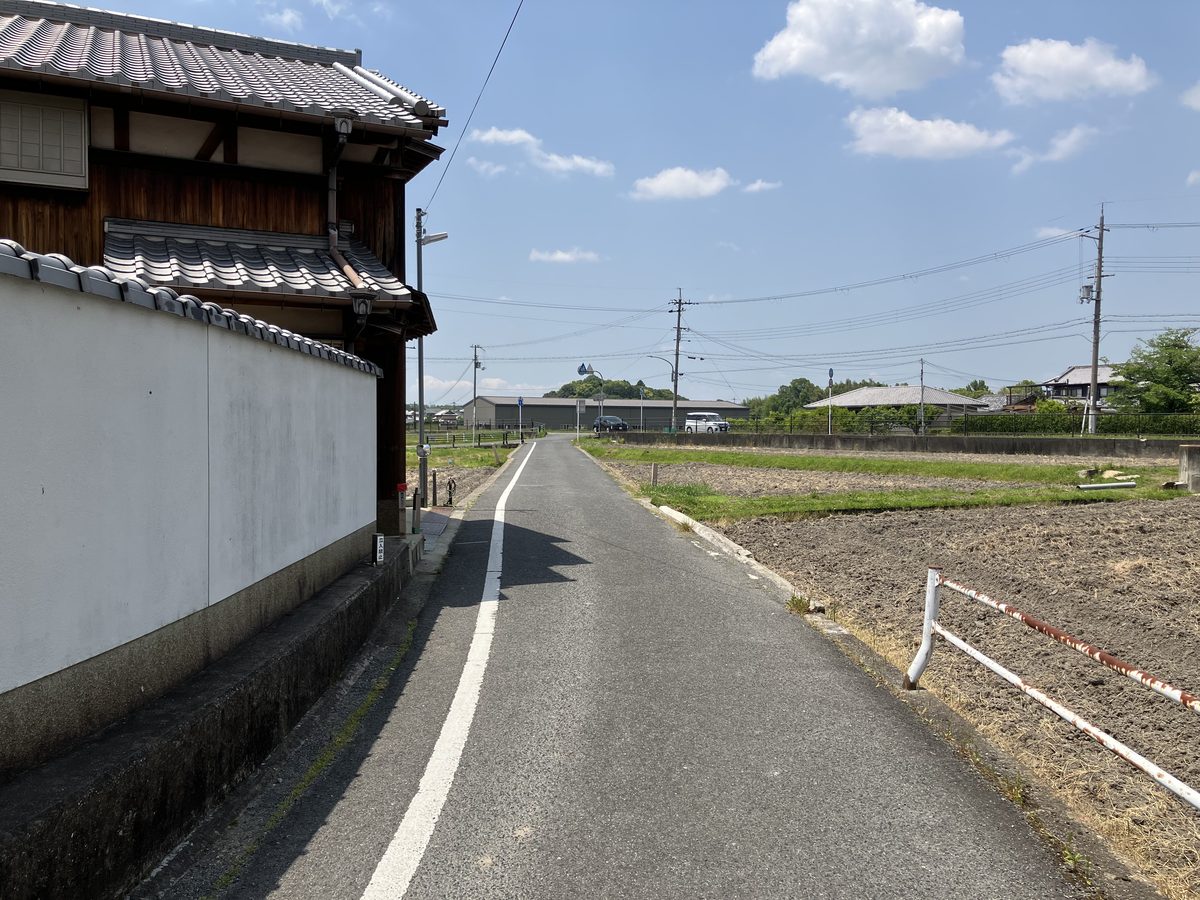 田んぼと民家の間の細い道を直進する