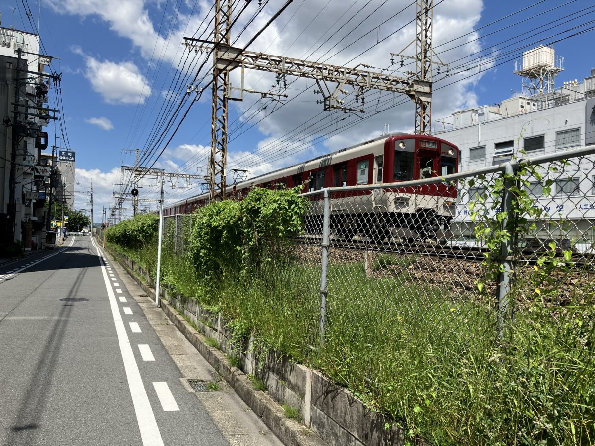 近鉄奈良線の電車が通過する線路沿いの道。赤い電車が見える