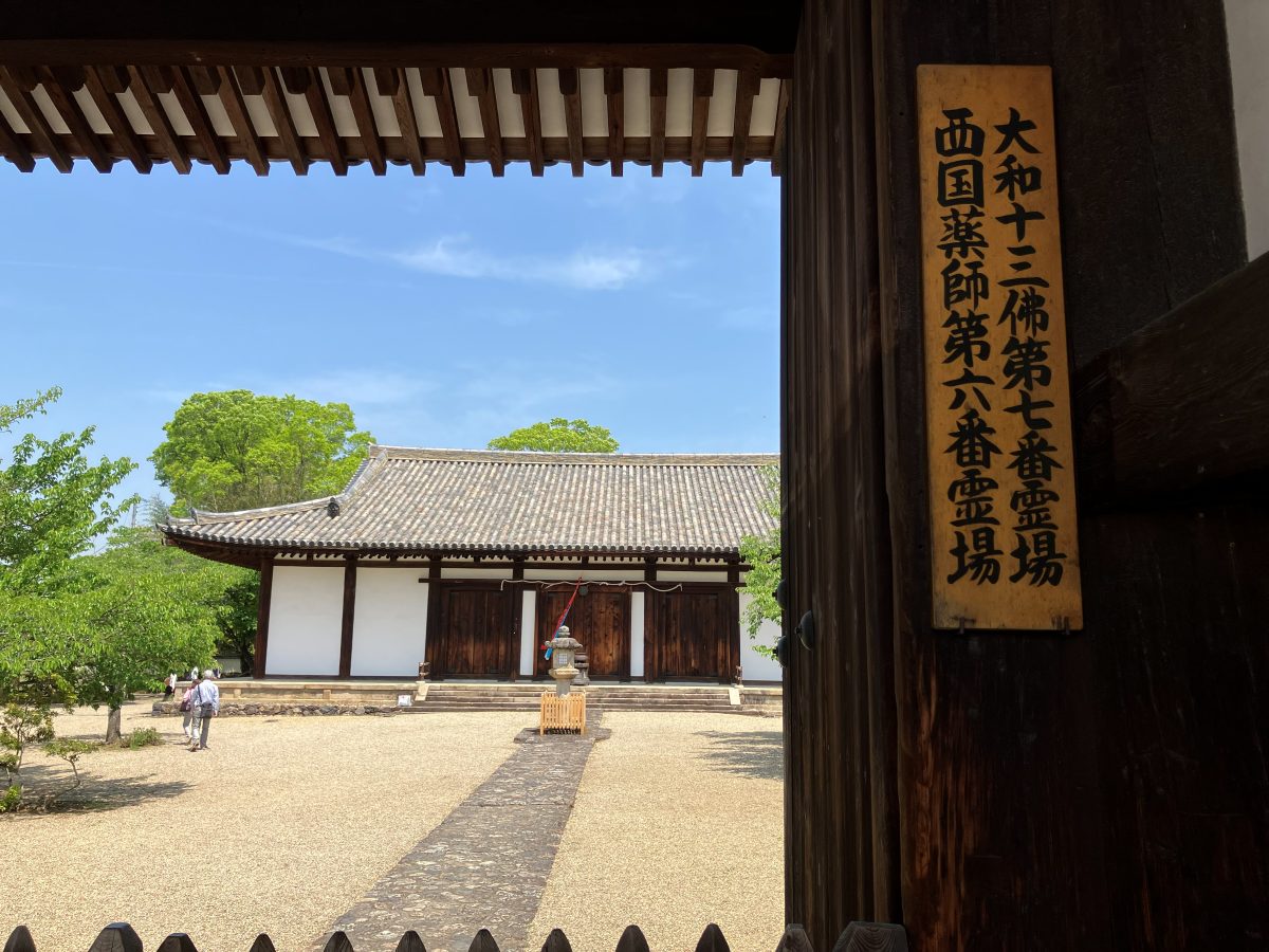 新薬師寺の南門越しに見る本堂 — 門の柱に西国薬師第六番霊場・大和十三佛第七番霊場の札